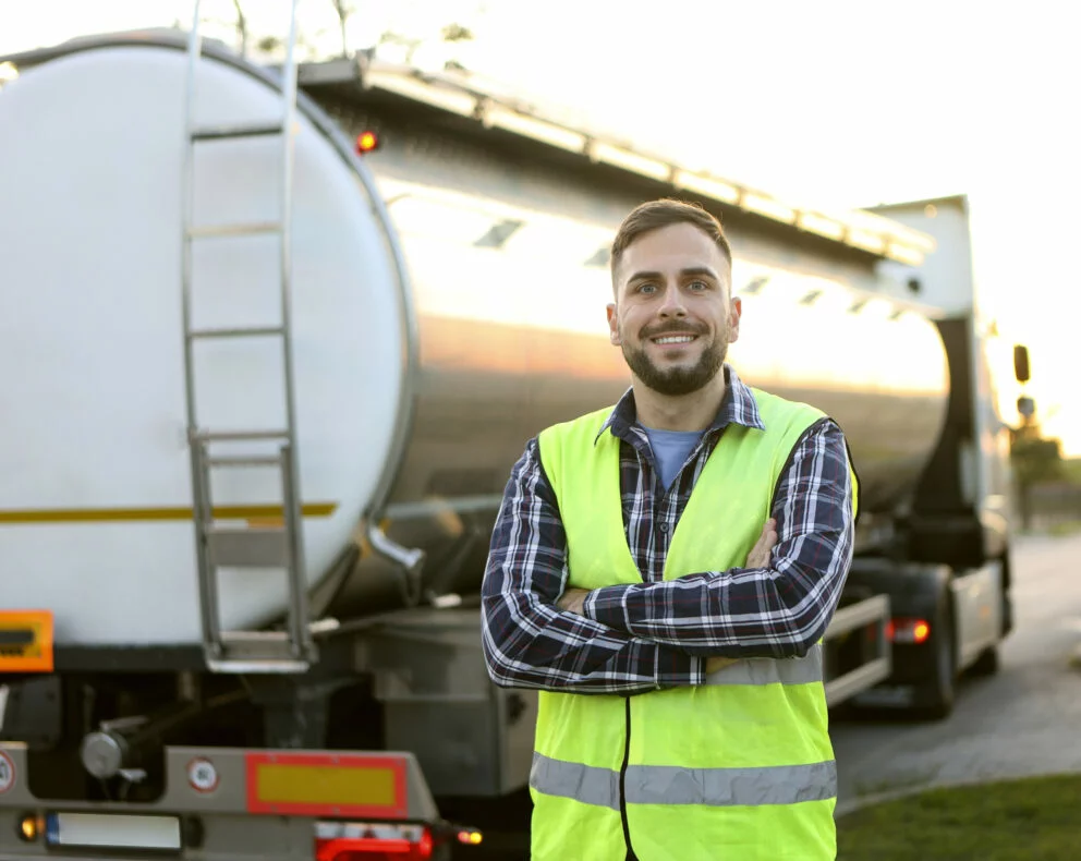 Chauffeur en gilet haute visibilité devant un camion‑citerne dédié au transport de produits pétroliers.